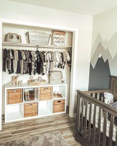 a baby's room with mountains painted on the wall and shelves filled with clothes