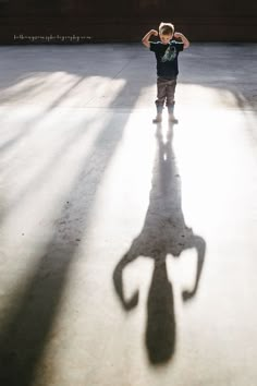 a young boy standing in the shadow of a building with his hands behind his head