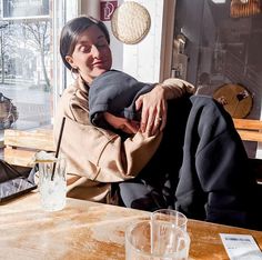 a woman sitting at a table in front of a window with her head on the pillow