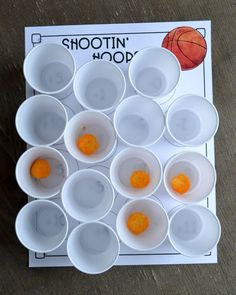 several white cups with orange balls in them on a wooden table next to a basketball game