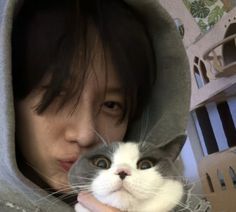 a woman holding a grey and white cat in front of her face while wearing a hoodie