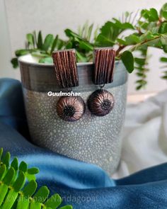 the earrings are made out of metal and have brown beads on them, sitting next to a potted plant