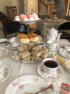 a table topped with plates and cups filled with sandwiches next to muffins on top of each other