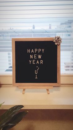 a sign that says happy new year next to a potted plant in front of a window