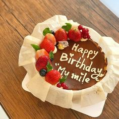 a birthday cake with strawberries and raspberries on it sitting on a table