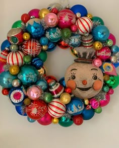 a christmas wreath with ornaments hanging on the wall and a face painted on it's side