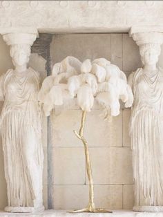 two statues with white feathers on them in front of a wall and a floor lamp