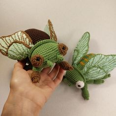 a hand holding a small crocheted toy with leaves on it's wings