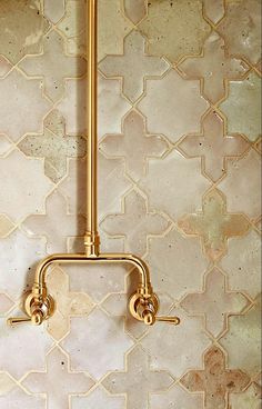 a gold faucet in the middle of a tiled wall with white and beige tiles