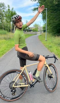 a woman riding on the back of a bike down a road with her arms in the air