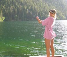 a woman standing on a dock with a fishing rod in her hand and trees in the background