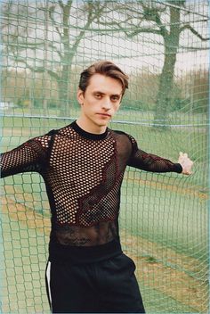 a man standing in front of a tennis net wearing black pants and a mesh shirt