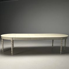 a white oval table with two legs and a curved top, in front of a gray wall