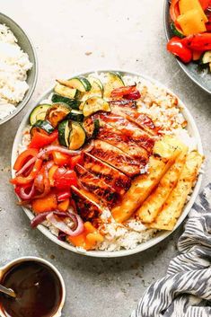 a white plate topped with chicken, rice and veggies next to bowls of sauce