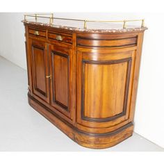 a wooden cabinet with marble top and brass trimmings on the bottom, sitting against a white wall