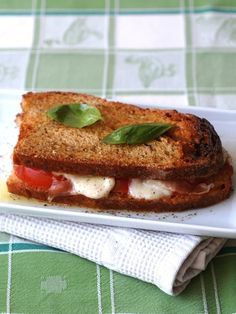 a grilled cheese and tomato sandwich on a white plate with a green checkered tablecloth