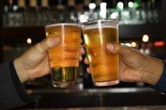 two people toasting with beer in front of a bar