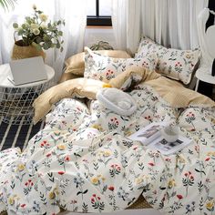 an unmade bed with flowers on it in a bedroom next to a window and potted plant