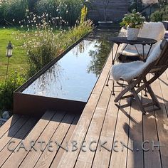 a wooden deck with a table and chairs next to a small pond in the middle of it