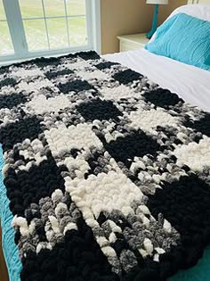 a crocheted black and white afghan on a bed with blue sheets, pillows and lamps