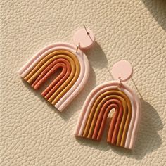 a pair of pink and yellow earrings on top of a white surface with circles hanging from it