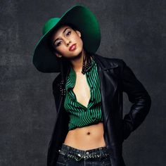 a woman wearing a green hat and black jacket posing for a magazine cover photo with her hands on her hips