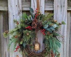 a wreath hanging on the side of a wooden fence with pine cones and evergreens