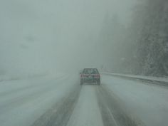 a car driving down a snow covered road in the middle of it's winter storm