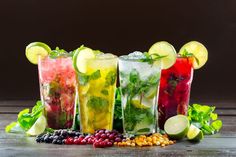 four glasses filled with different types of drinks and garnished with limes, raspberries, lemon slices, and mint