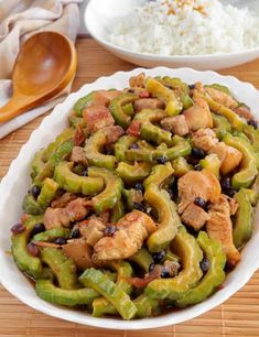 a white bowl filled with green peppers and chicken next to rice on a wooden table