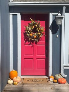 a red door with a wreath and pumpkins on the front step next to it