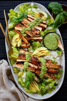 a salad with chicken, avocado and cilantro dressing on it next to a spoon