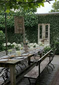 an outdoor dining table set with place settings for six people, surrounded by greenery