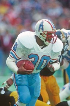 a football player running with the ball in his hand and other players on the field behind him