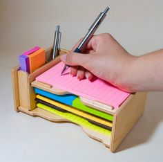 a person's hand holding a pen and writing on top of a stack of sticky notes