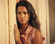 a woman leaning against a wall with her hands on her chest and looking at the camera