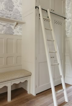 a white ladder leaning against the wall next to a bench with a cushion on it