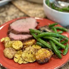 a red plate topped with meat, potatoes and green beans