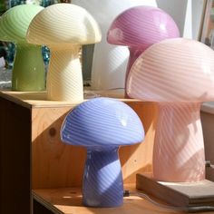 three different colored lamps sitting on top of a wooden table next to each other in front of a window