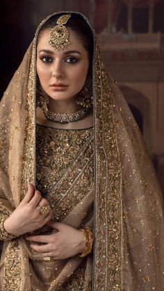 a woman wearing a gold and silver bridal outfit with her hands on her chest