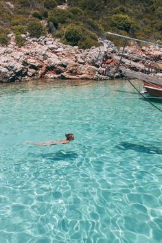 a man swimming in the ocean next to a boat and some rocks on the shore