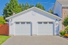 two white garages in front of a house with trees and flowers on the side