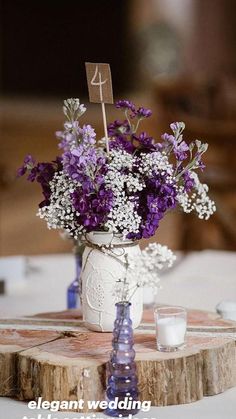 purple and white flowers in a mason jar on a wooden slice at a wedding reception