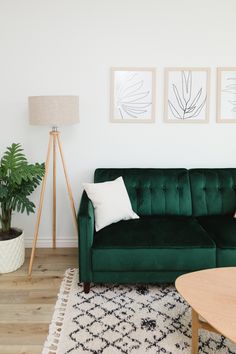 a living room with a green couch and two paintings on the wall above it's coffee table