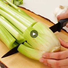 a person cutting up celery on top of a wooden cutting board with a knife