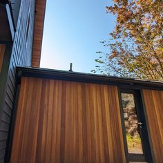 the side of a house that has wooden siding on it and is next to a tree