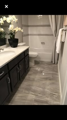 a bathroom with white flowers in a black vase on the counter and gray tiles on the floor