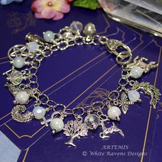 a silver bracelet with charms on it sitting on top of a purple table next to flowers