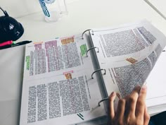 a person is holding a pen and looking at a book on a table with papers