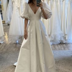 a woman taking a selfie while wearing a white dress in front of wedding gowns